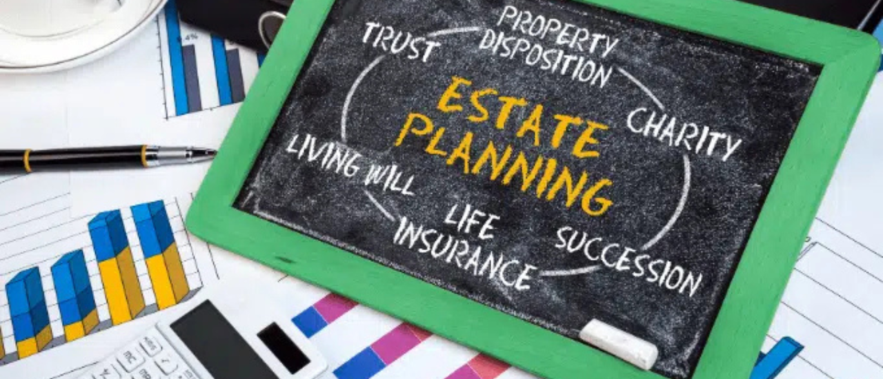 Chalkboard displaying "Estate Planning" surrounded by related terms like Wills, Trusts, Probate, Property Disposition, Life Insurance, and Succession, on a desk with financial charts.
