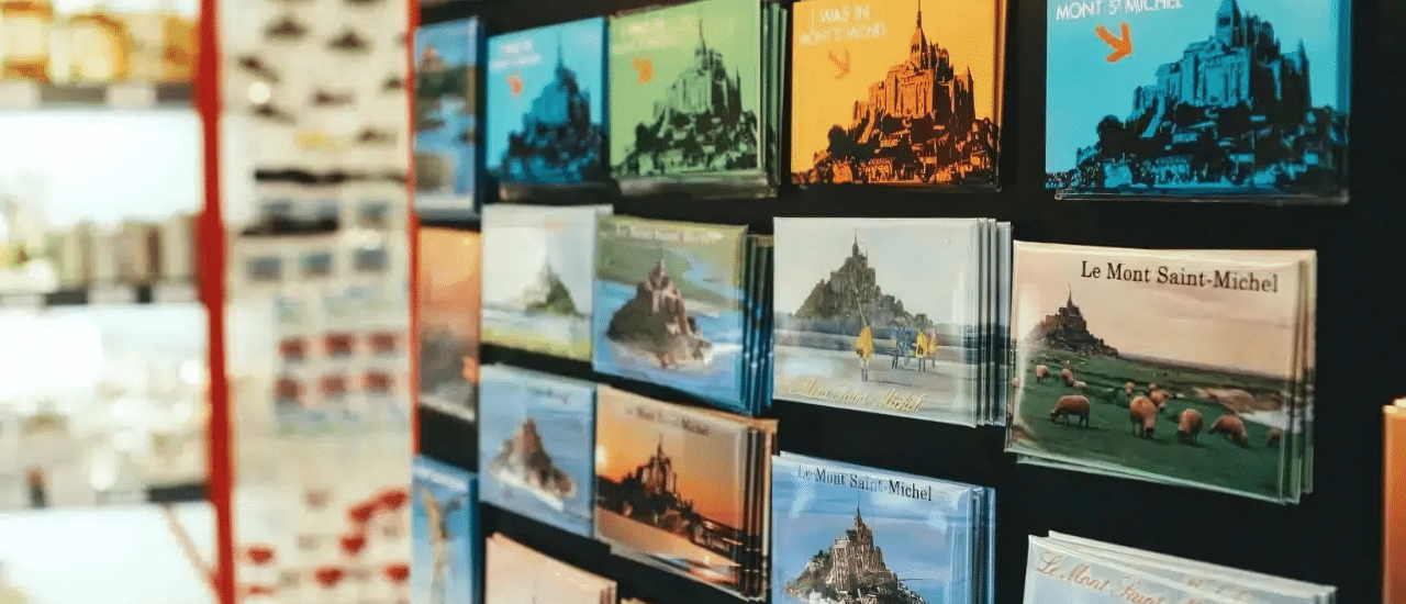A display rack filled with various postcards featuring illustrations of Mont Saint-Michel, symbolizing direct mail pieces ready for tracking and optimization.