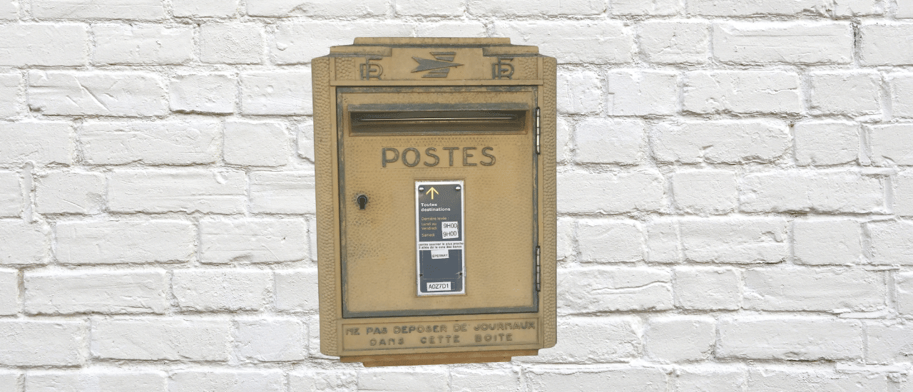 A vintage French "Postes" mailbox mounted on a white brick wall, symbolizing traditional and effective direct mail communication.
